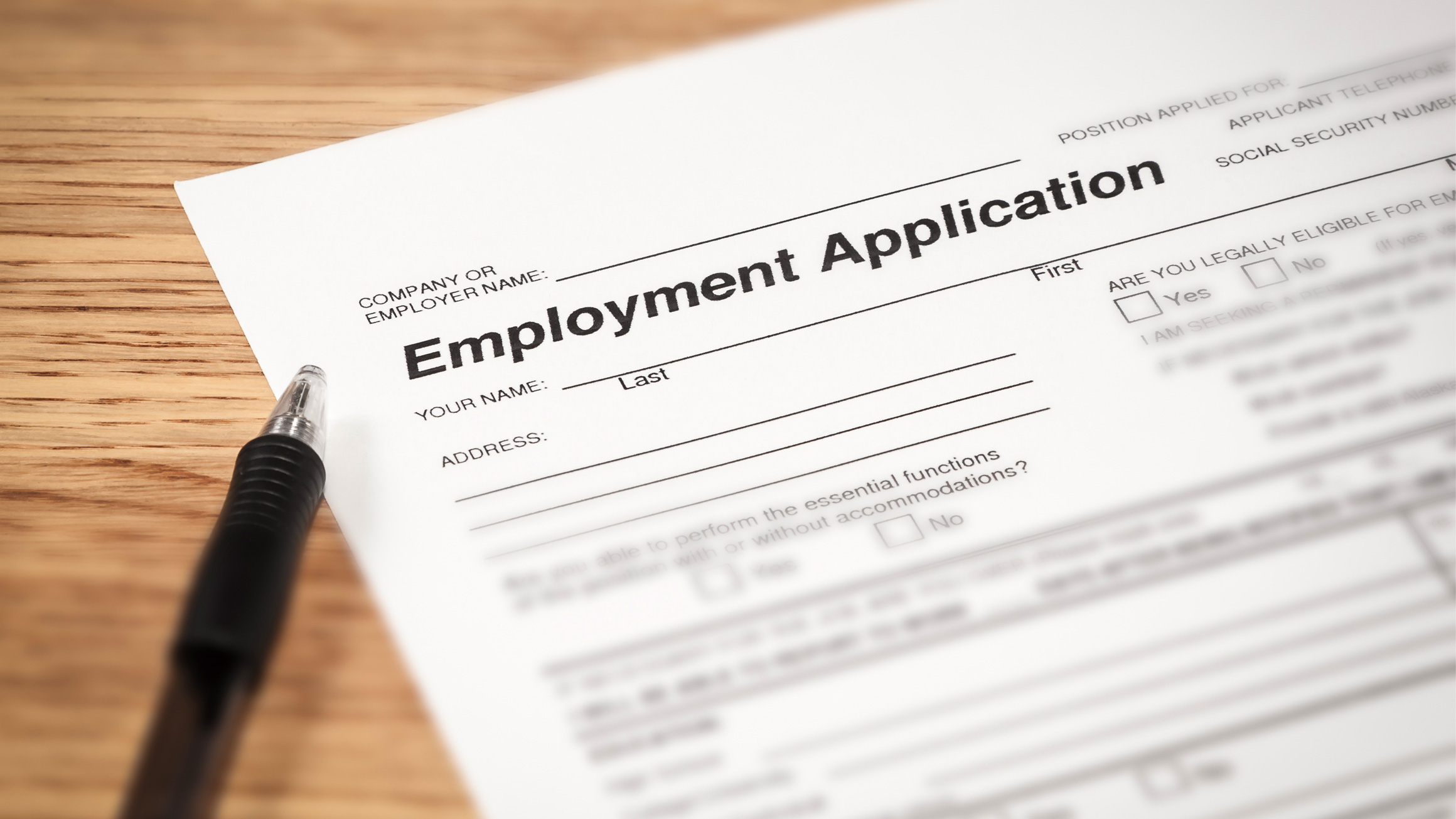 An employment application is shown with a pen on a wooden surface