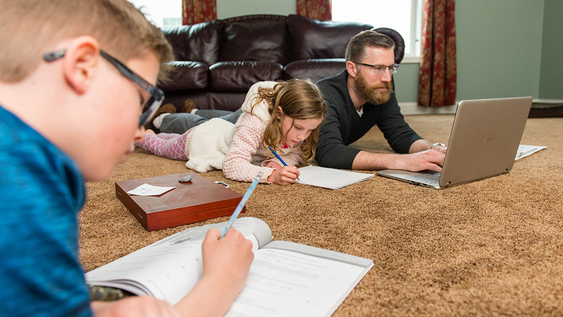 Aaron Spak on the floor, working at his computer, with his children