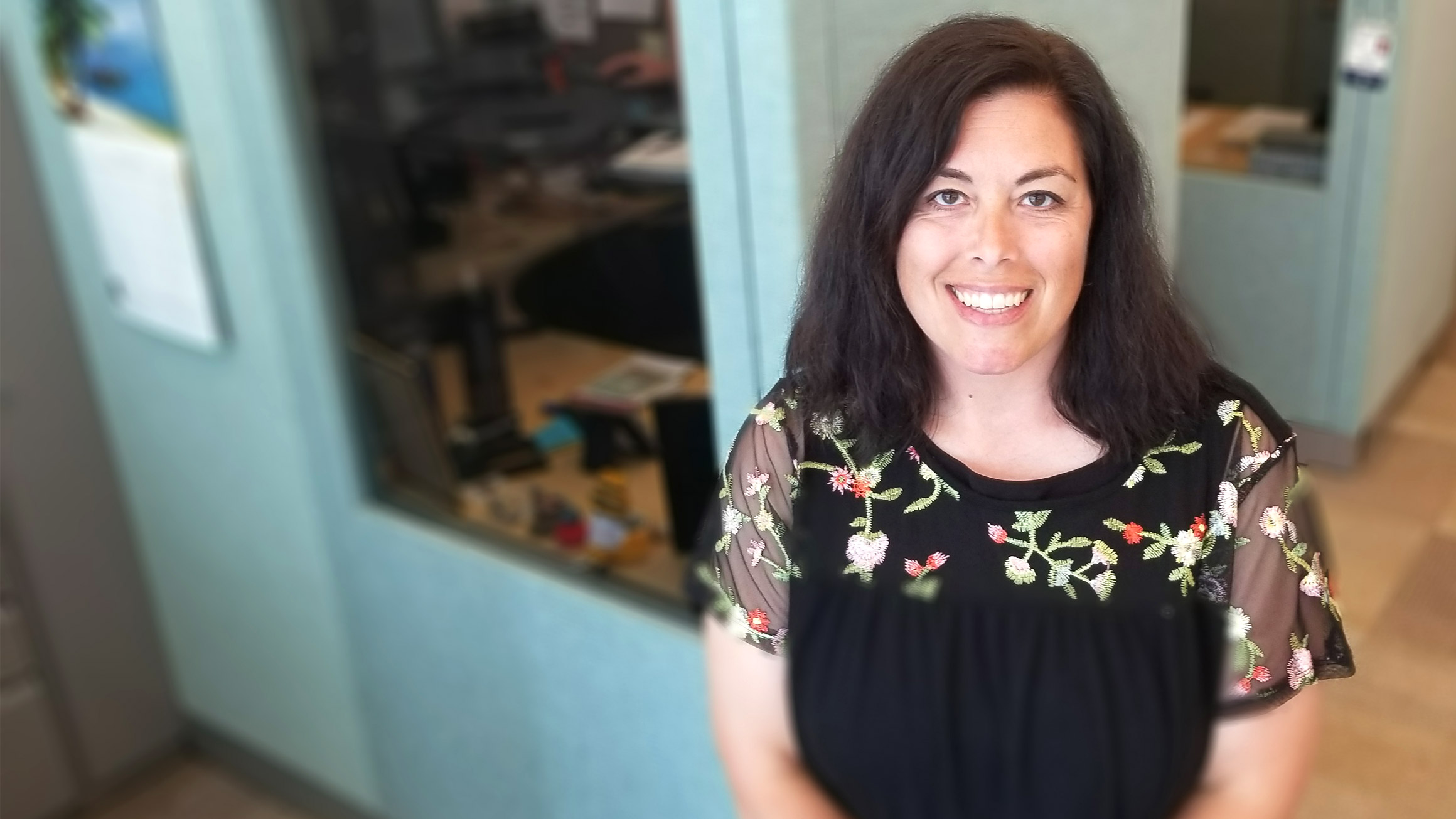 Dawn Coder, the director of academic advising and student disability services, stands to the right side of the photo with the walls of a cubicle behind her.