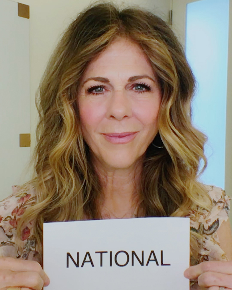 Actress Rita Wilson holds up a sheet of paper that has the word "National" on it.