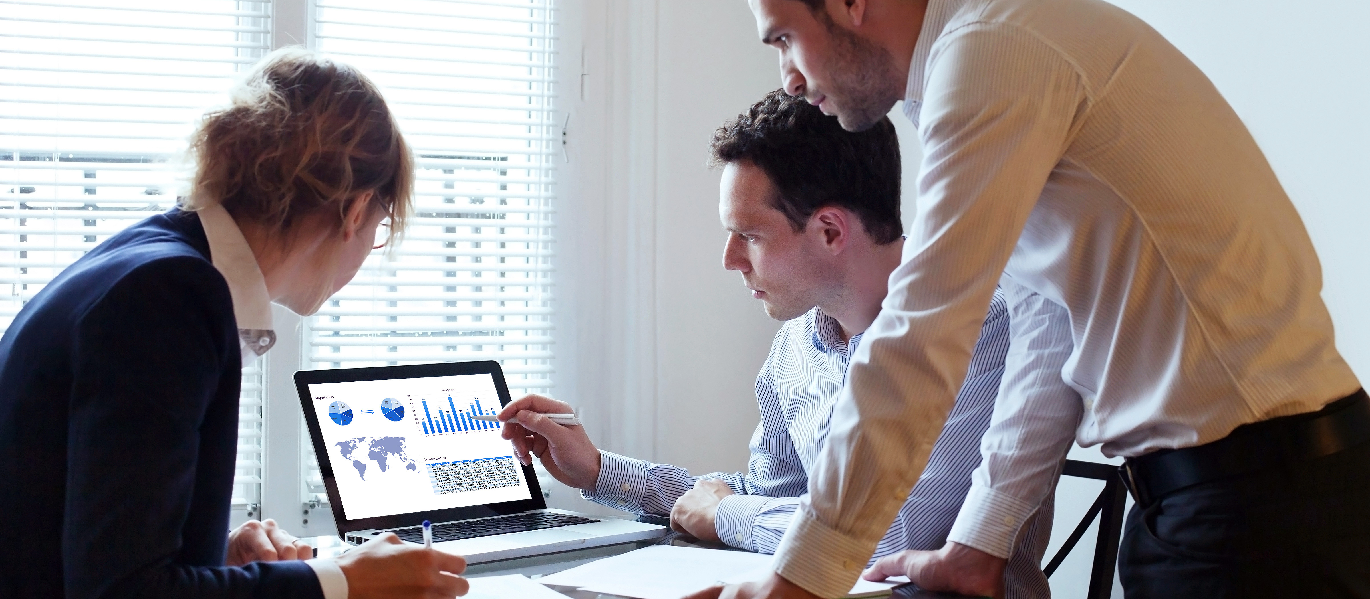 Three professionals gathered around a computer reviewing information