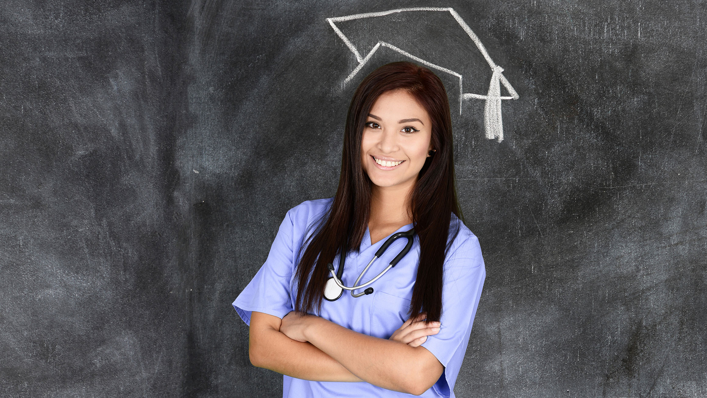  A nurse stands behind a chalkboard with a graduation cap on the chalkboard