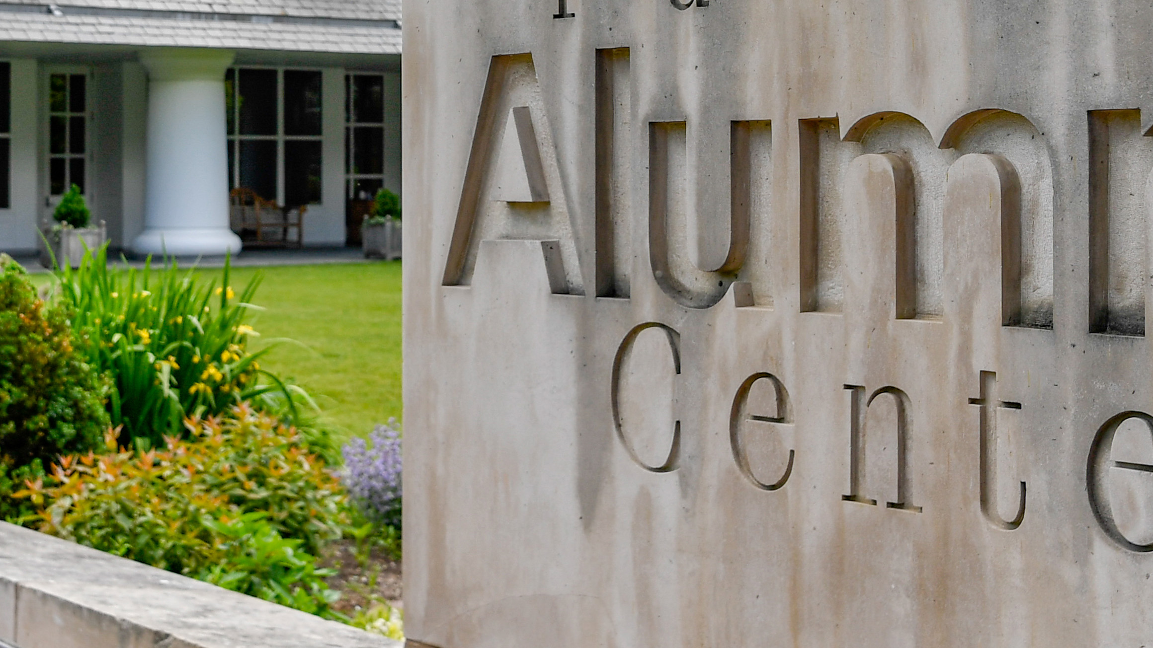 The sign Alumni Center is shown on a stone wall in a garden