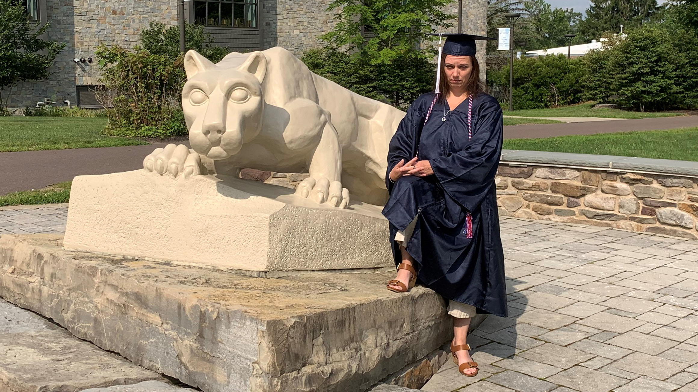 Jessica Butler is wearing a Penn State cap and gown at a Nittany Lion statue