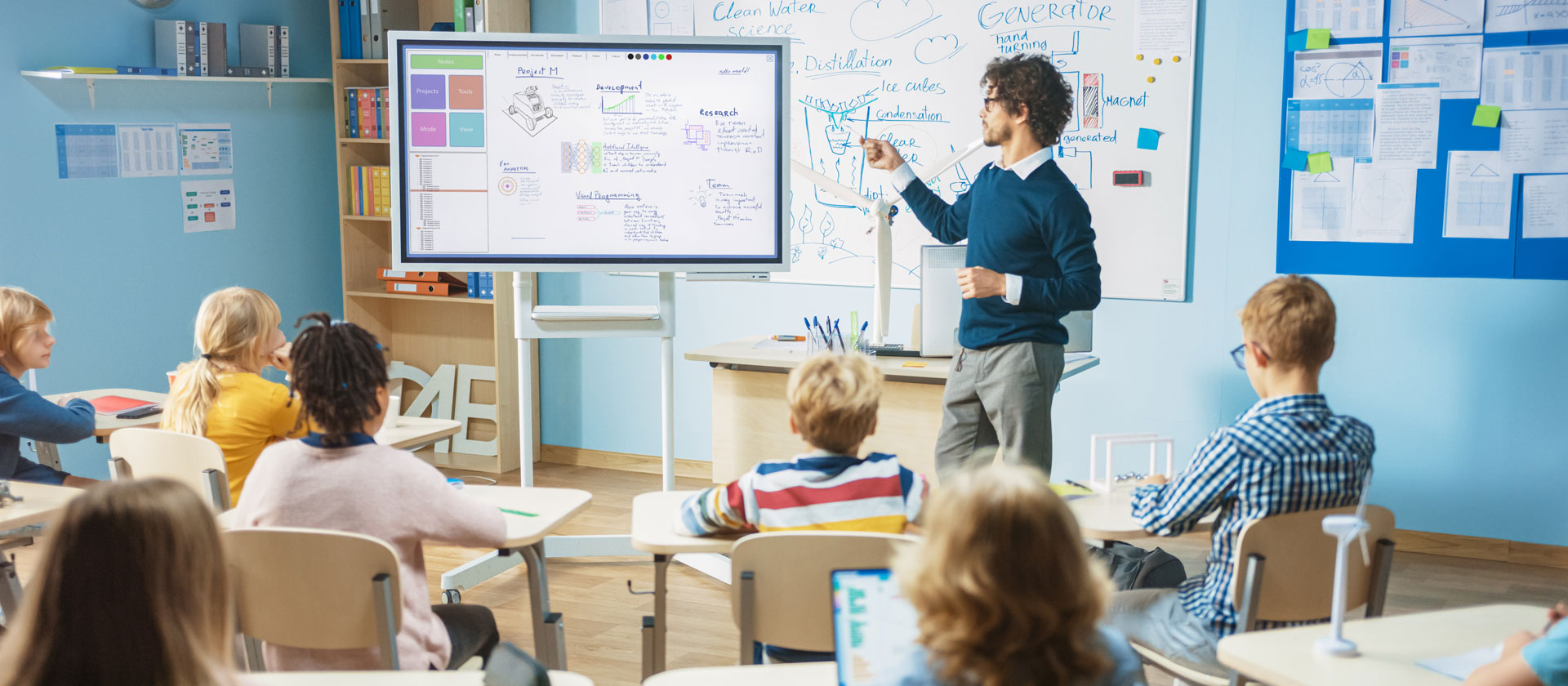Teacher pointing to lesson on a smart board in front elementary class