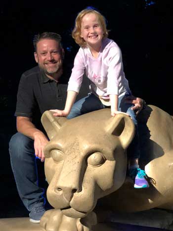 Artie Cressman poses with his daughter, who is sitting on the Nittany Lion shrine