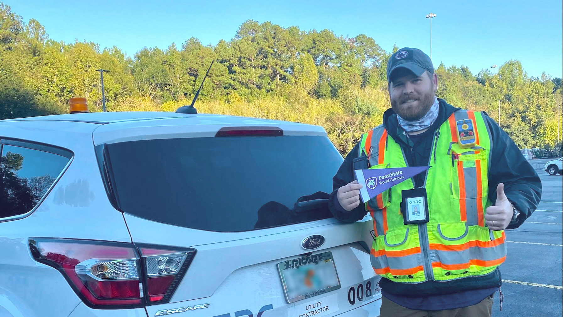 Alex Swithers holds a Penn State World Campus pennant while standing behind a white Ford