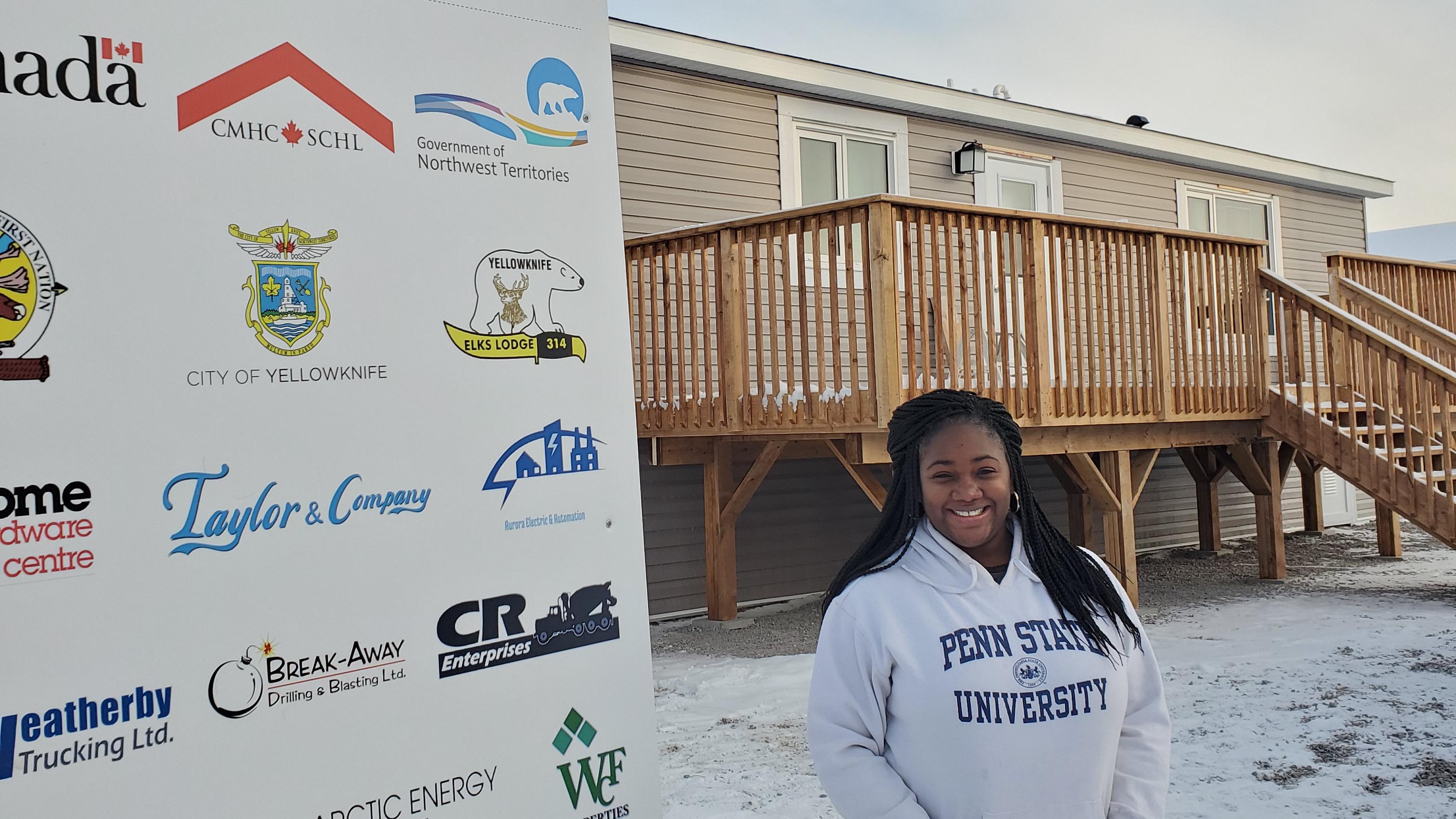 Miriam Pallard stands in front of a home built through Habitat for Humanity. She is wearing a sweatshirt with the words "Penn State University" on it.