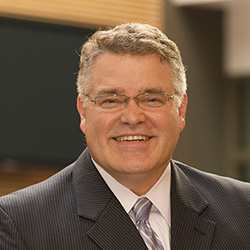 A headshot of Chris Calkins, who is wearing a suit jacket and a tie