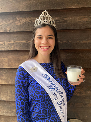 Mikayla Davis wears a crown and sash while holding a glass of milk.