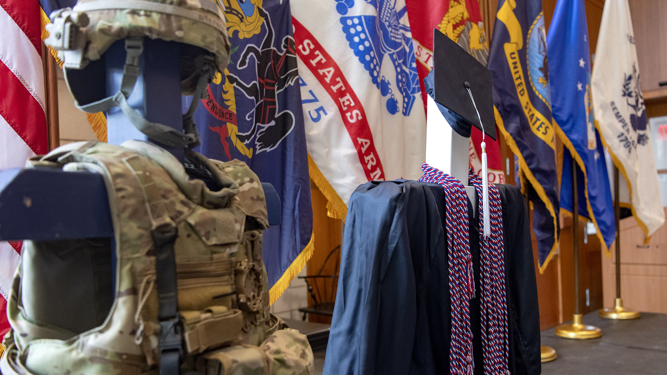 A graduation gown with military honor cords is shown next to military gear