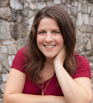 A woman poses in front of a stone wall.