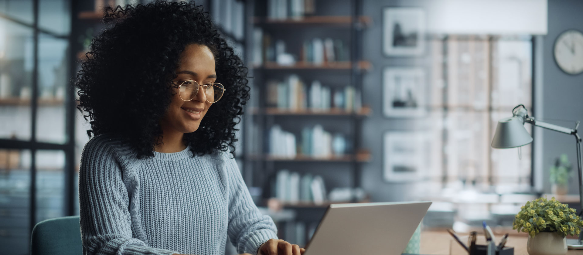 woman with glasses and curly black hair works on laptop