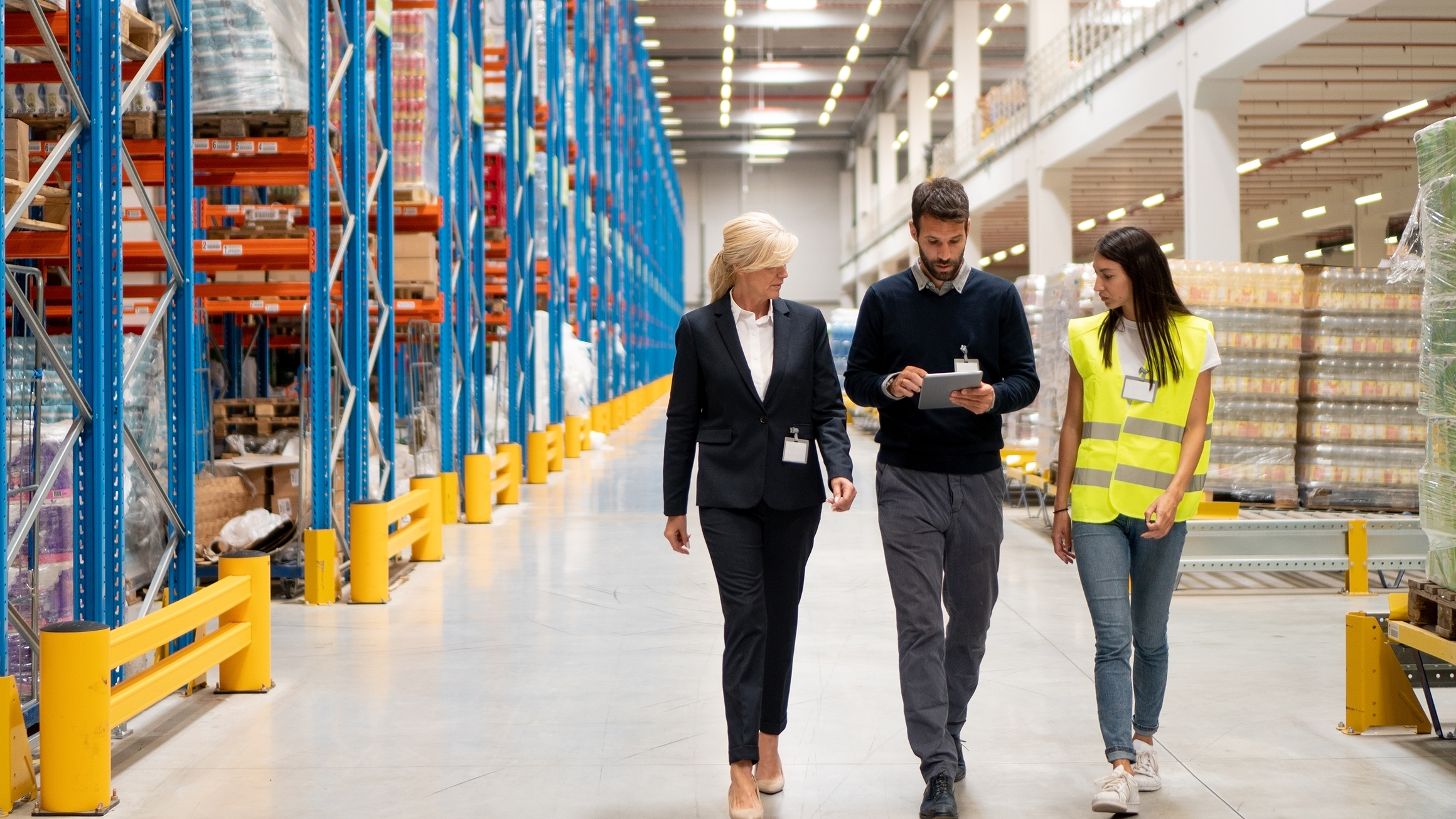 Three people walk in a warehouse.