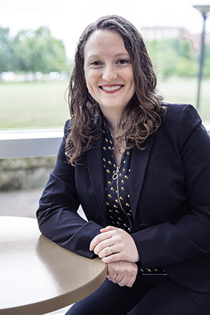 Lex Shawbaker sits at a round table with a window in the background. She's wearing a business suit.