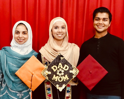 Three people pose with graduation capts.