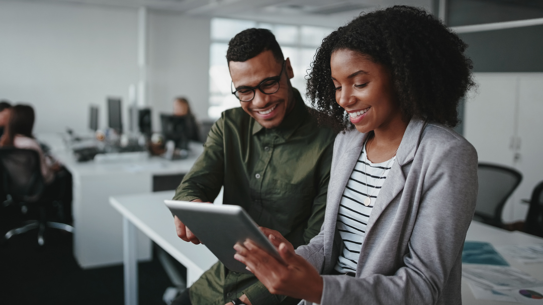 Two business professionals reviewing work on a tablet in an office setting