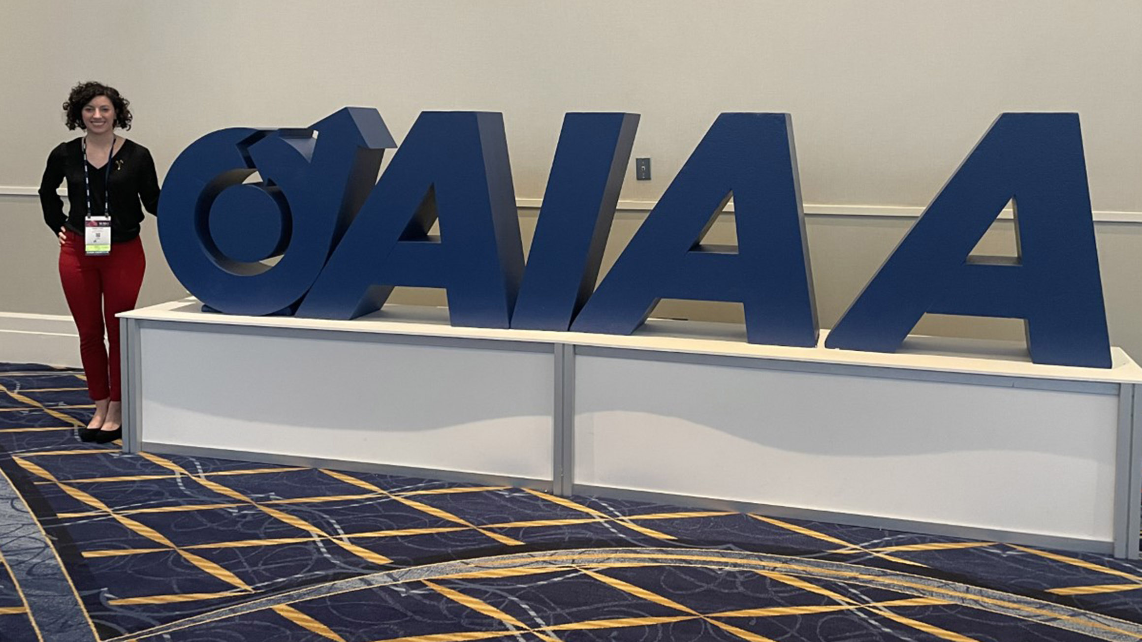 Renee Dorer stands next to a blocks spelling out the acronym AIAA in a conference room