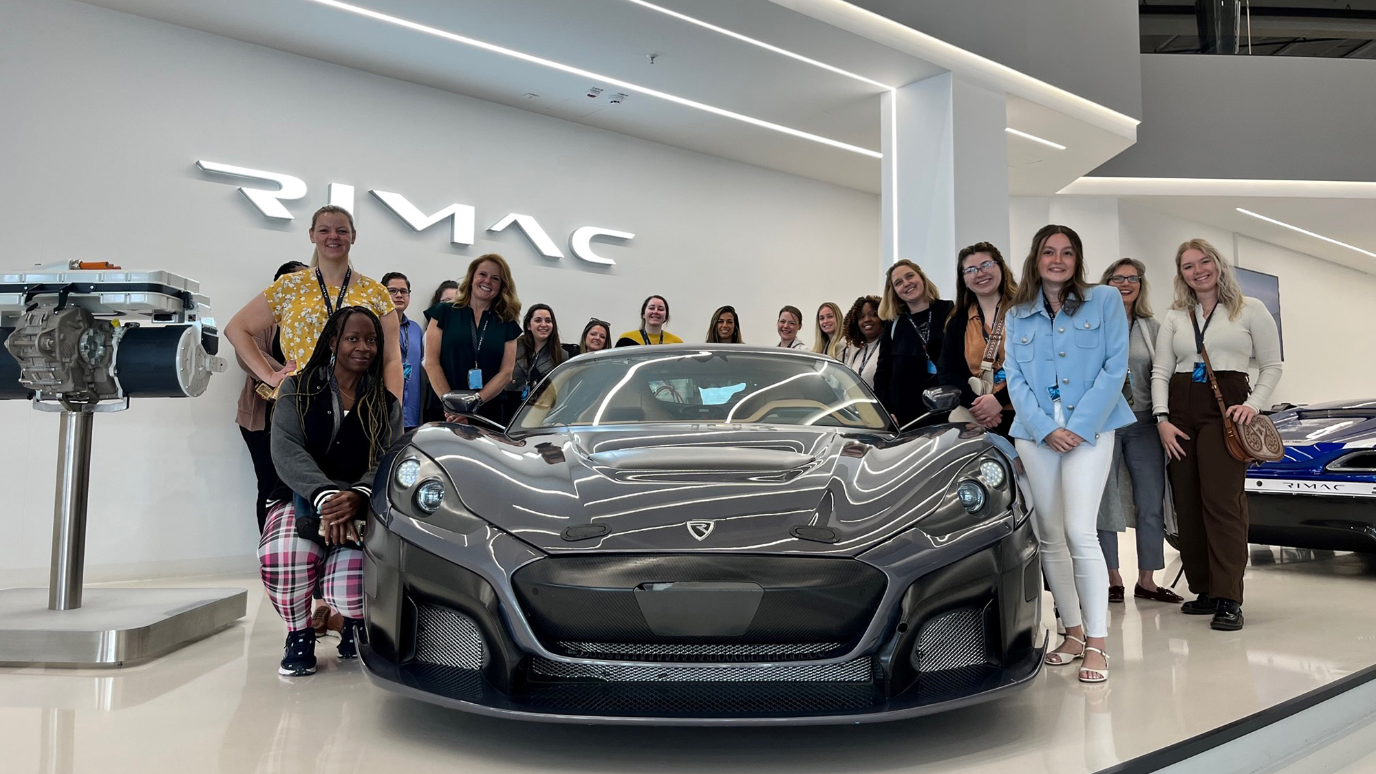 A group of people pose around a car.