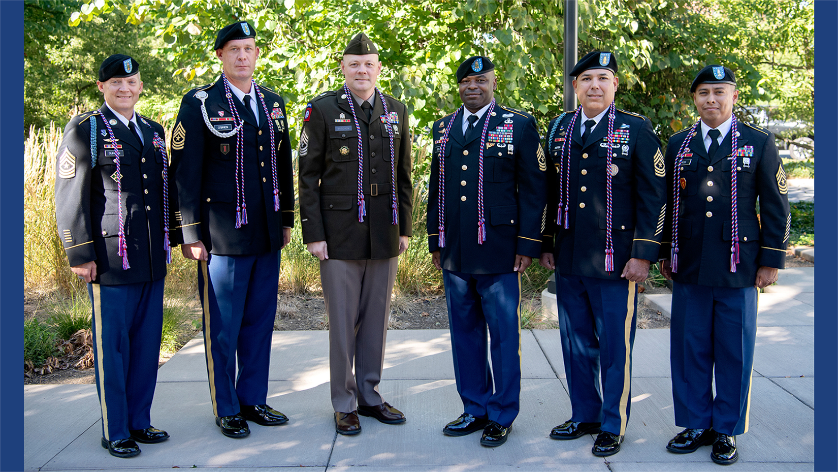 Six men in dress military uniforms pose outside.