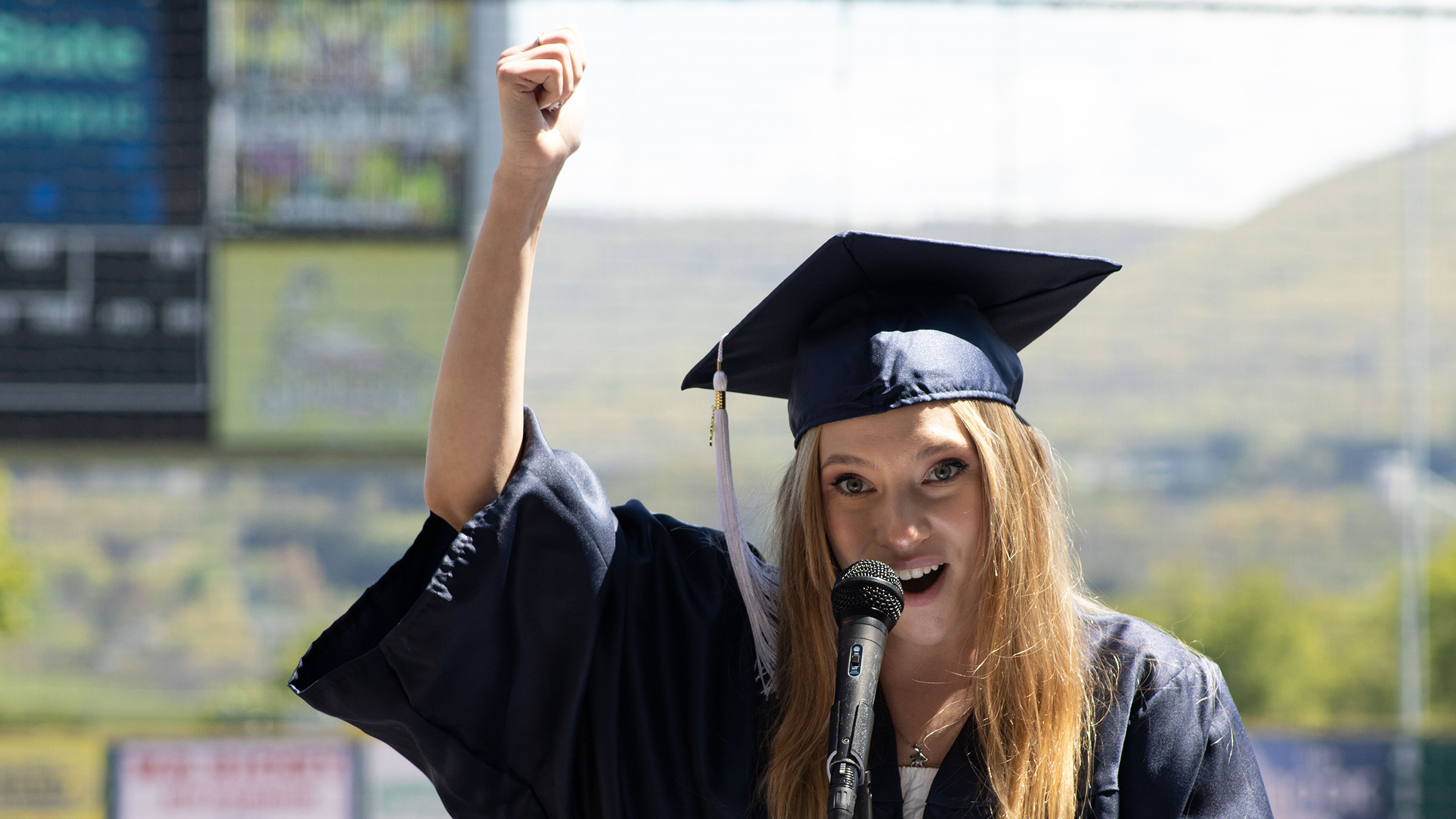 A woman in a graduation cap and gown holds a first in the air.