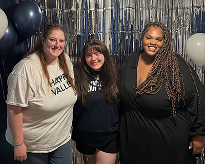 Three people pose in front of a shimmery silver background.