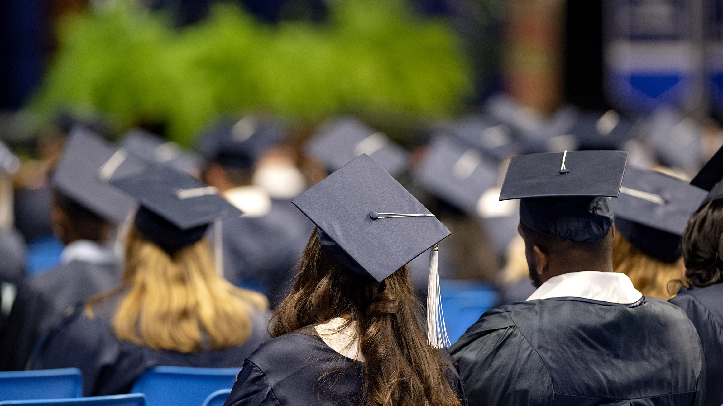 Students wearing graduation caps and gowns sit in chairs waiting to hear their names read during a commencement ceremony