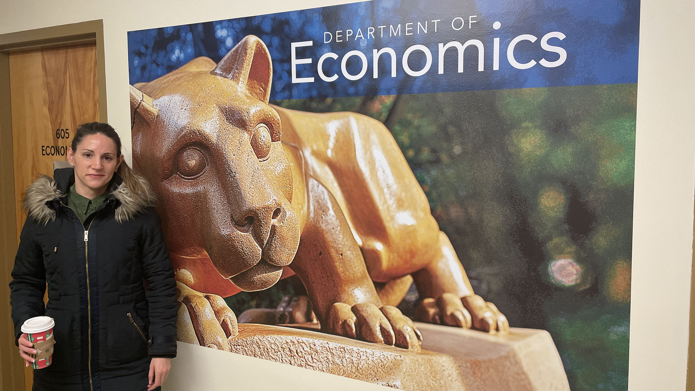 Marian Viera Fuentes stands to the left of the sign for the Department of Economics