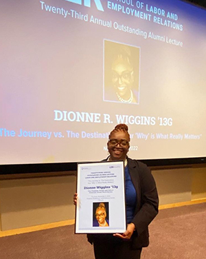 Dionne Wiggins poses in front of a presentation screen holding a framed poster.