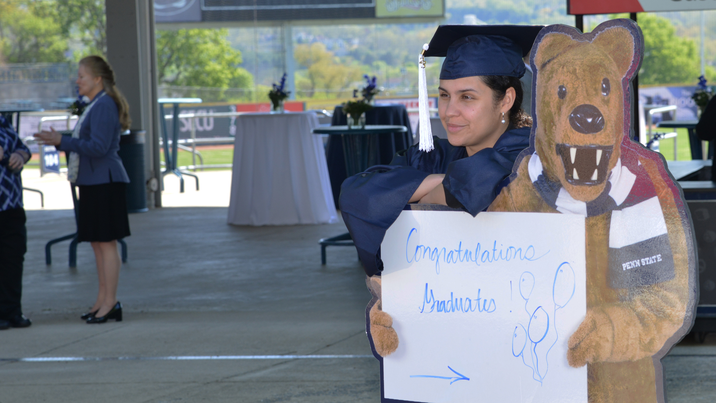 A woman stands in a blue cap and gown posing with a Nittany Lion cutout.