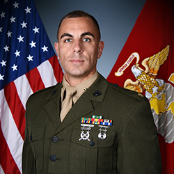 Andrew Budzien in his military uniform flanked by a U.S. flag and a Marine Corps flag in the background