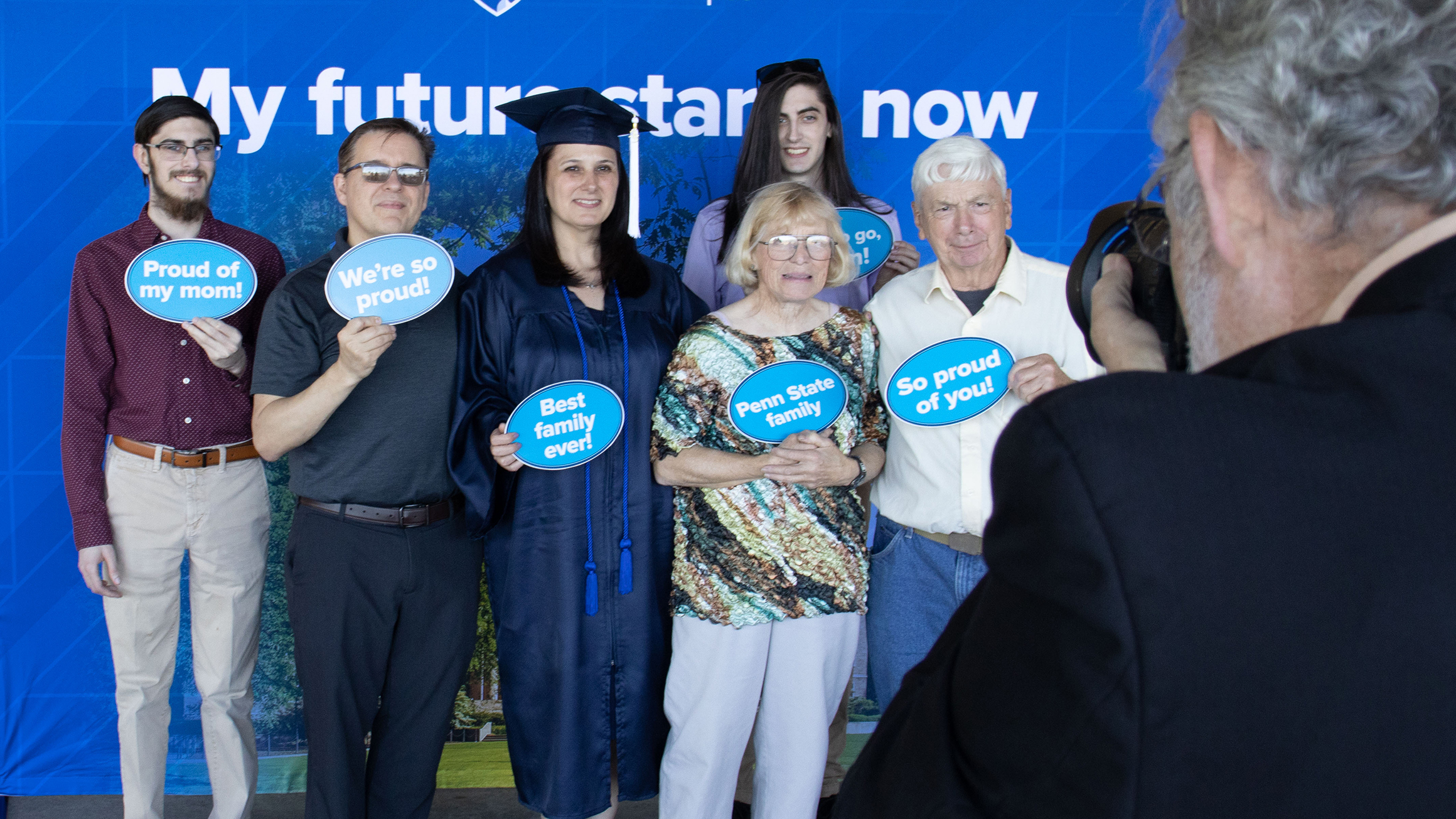A photographer takes a picture of a family with a grad in a cap and gown.
