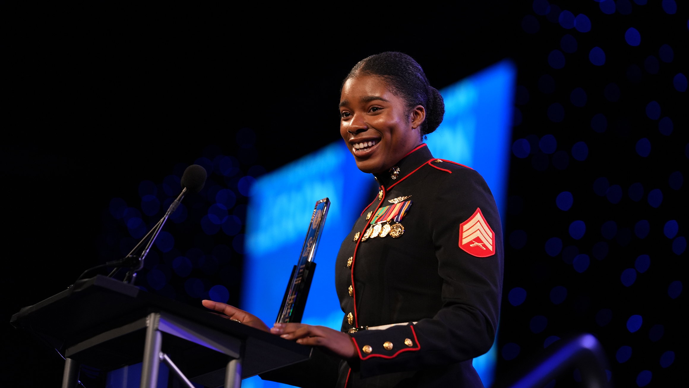A woman in a military uniform stands at a podium and speaks to an audience.