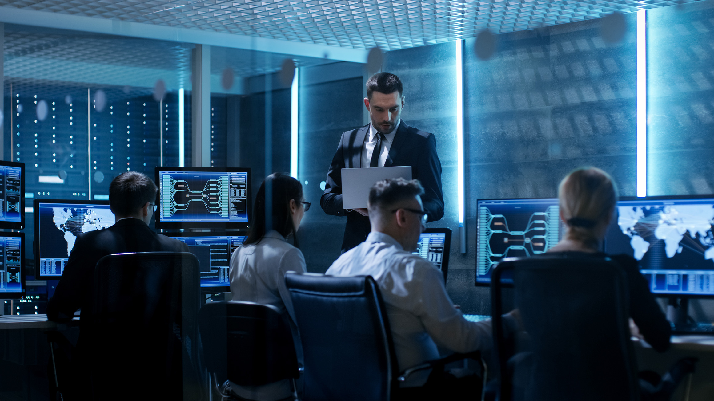 A group of people work at computers in a technological office setting.