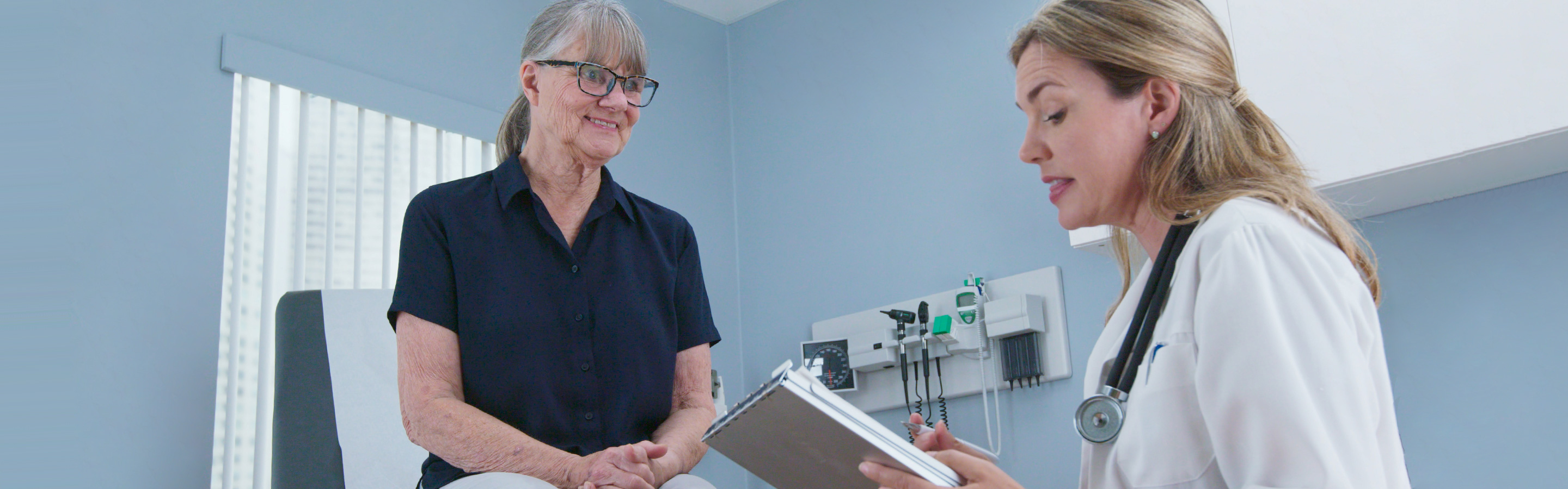 Female medical professional talks to patient on exam table.