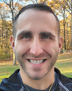 A headshot photo of a man standing in a wooded area.