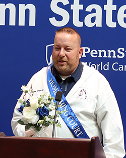 A man stands at a podium in front of a Penn State background.