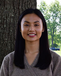 A woman stands in front of a tree.