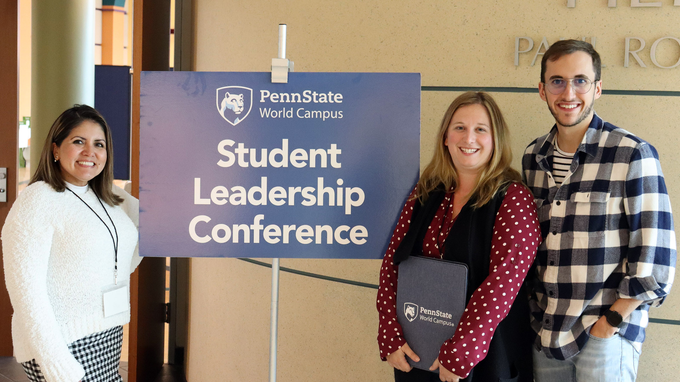Three students flank the sign "Penn State World Campus Student Leadership Conference"