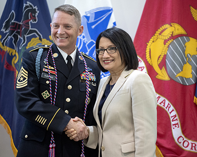 A man wearing a military uniform shakes a woman's hand.