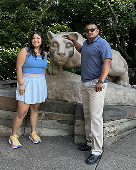 A man and woman stand in front of a rocky area and lion sculpture.