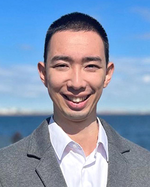 A man wearing a suit stands in front of water.