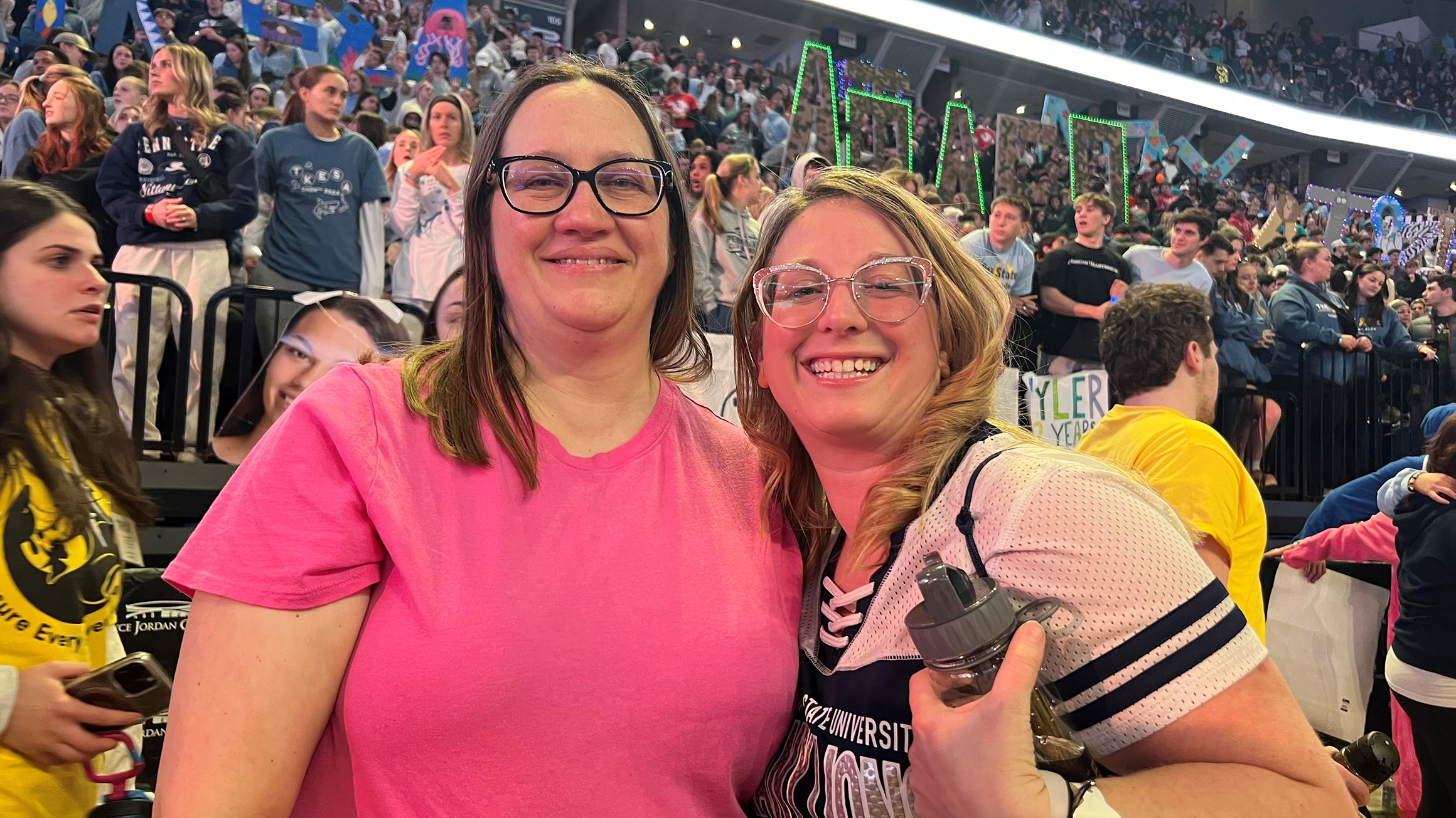 Two women pose in a crowded arena.