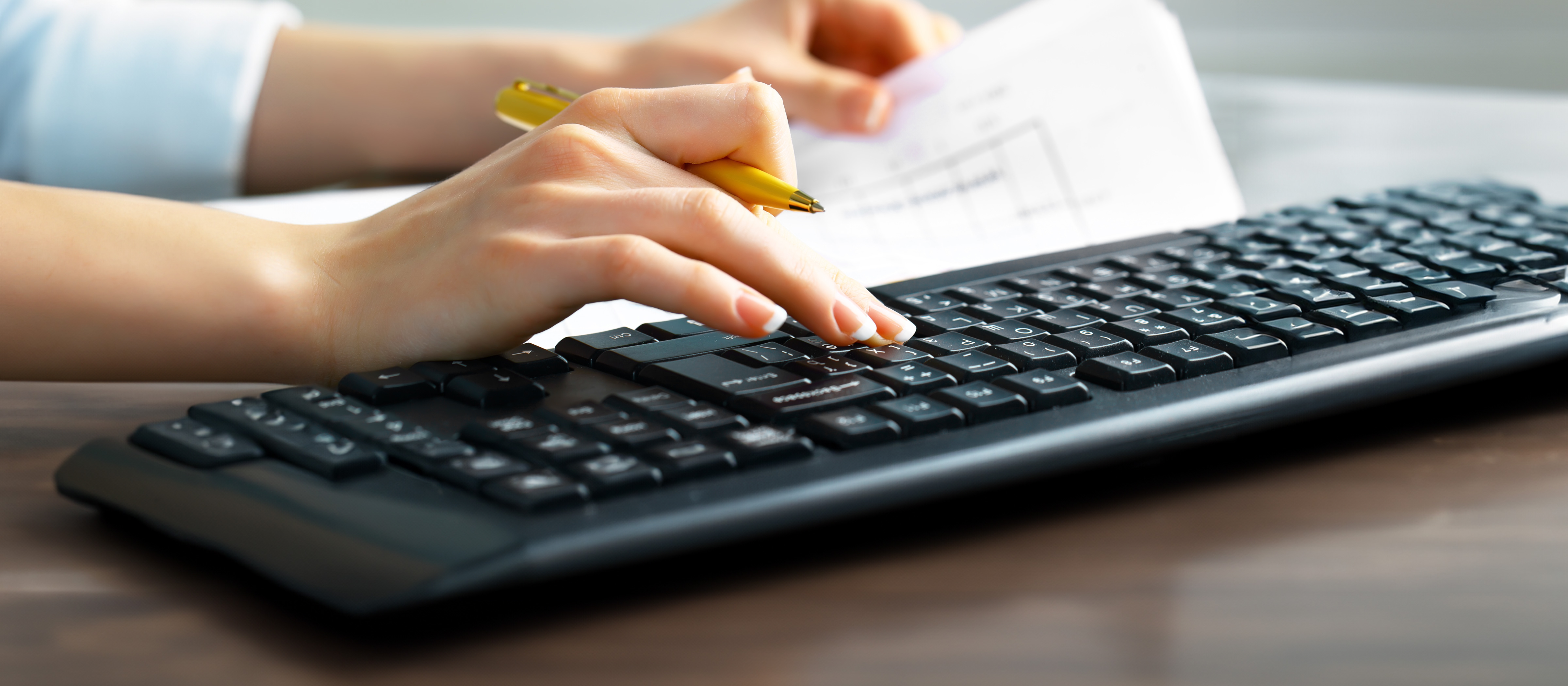 close up of a hands holding a pen and typing on a keyboard