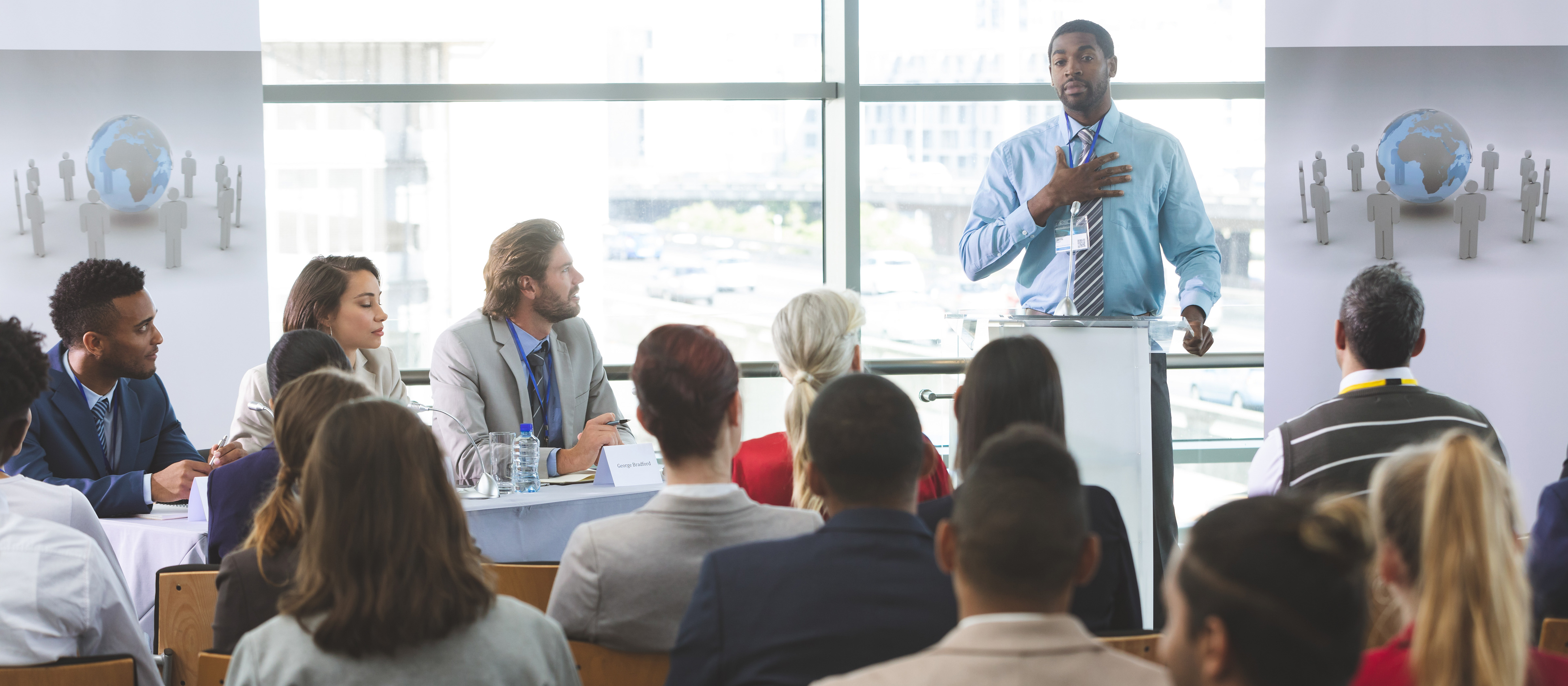 Man standing at a podium speaking to a room full of people 