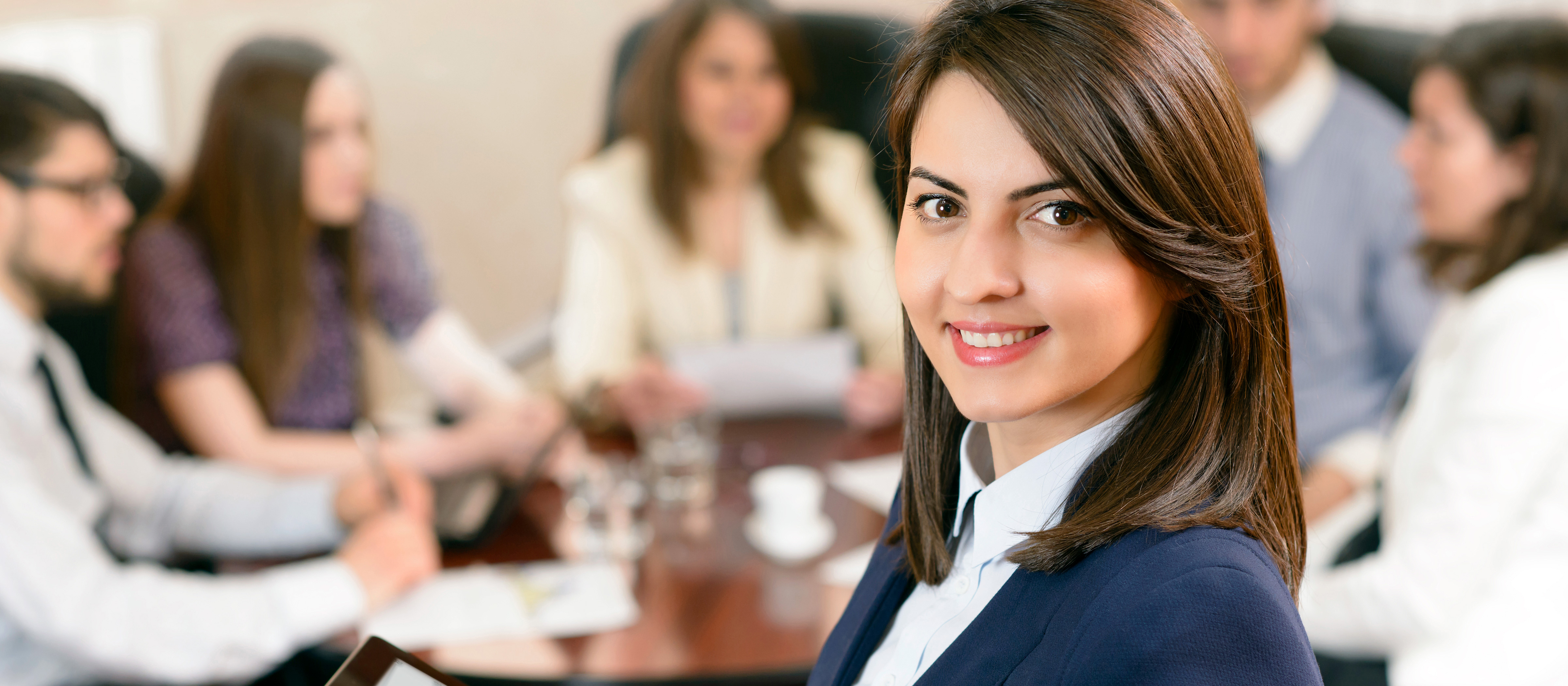 business woman smiling at the camera while sitting at a conference table 