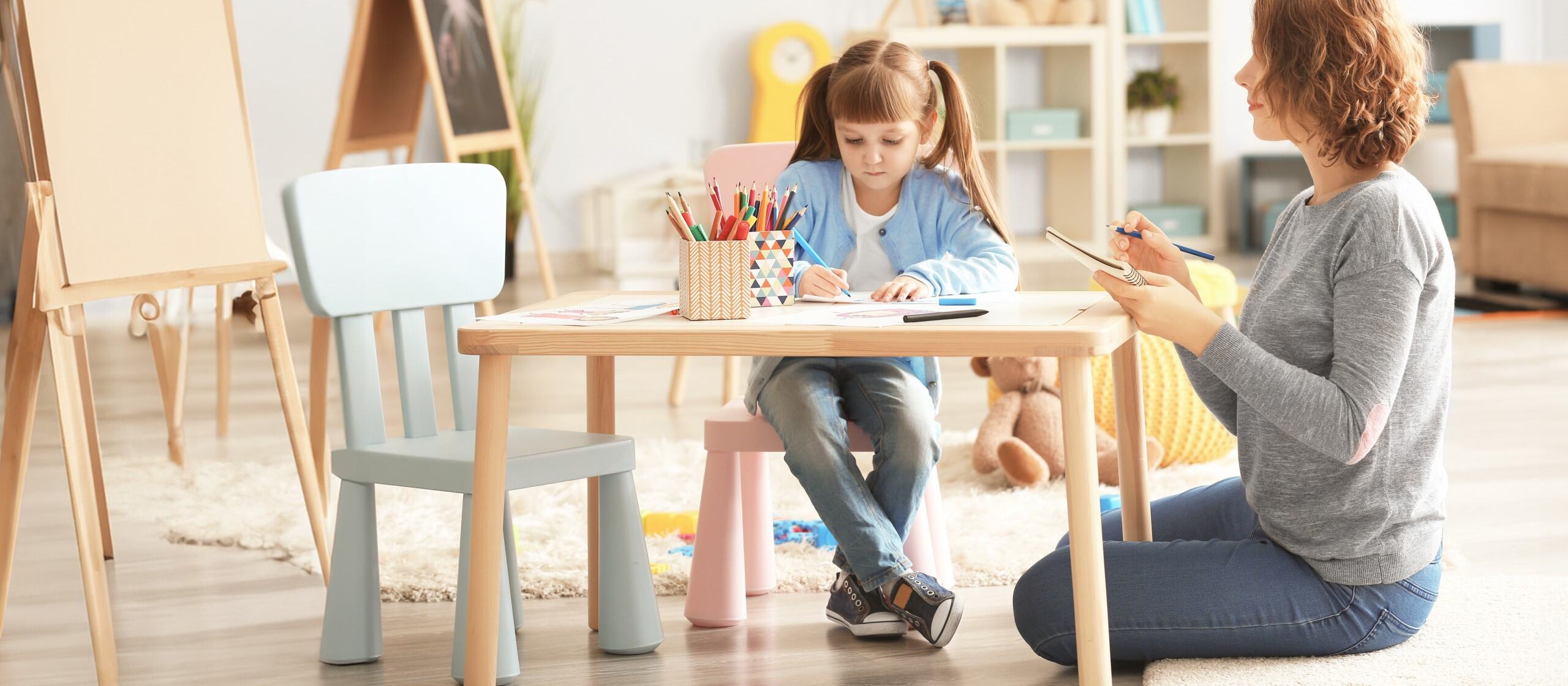 woman sitting at a small table while a child colors