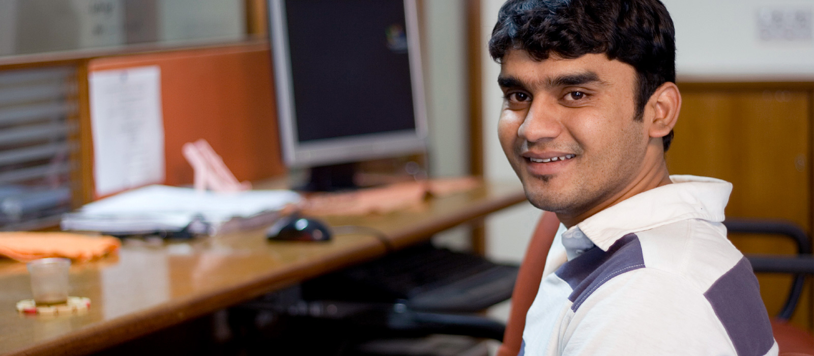 man smiling at the camera while sitting on the desk 