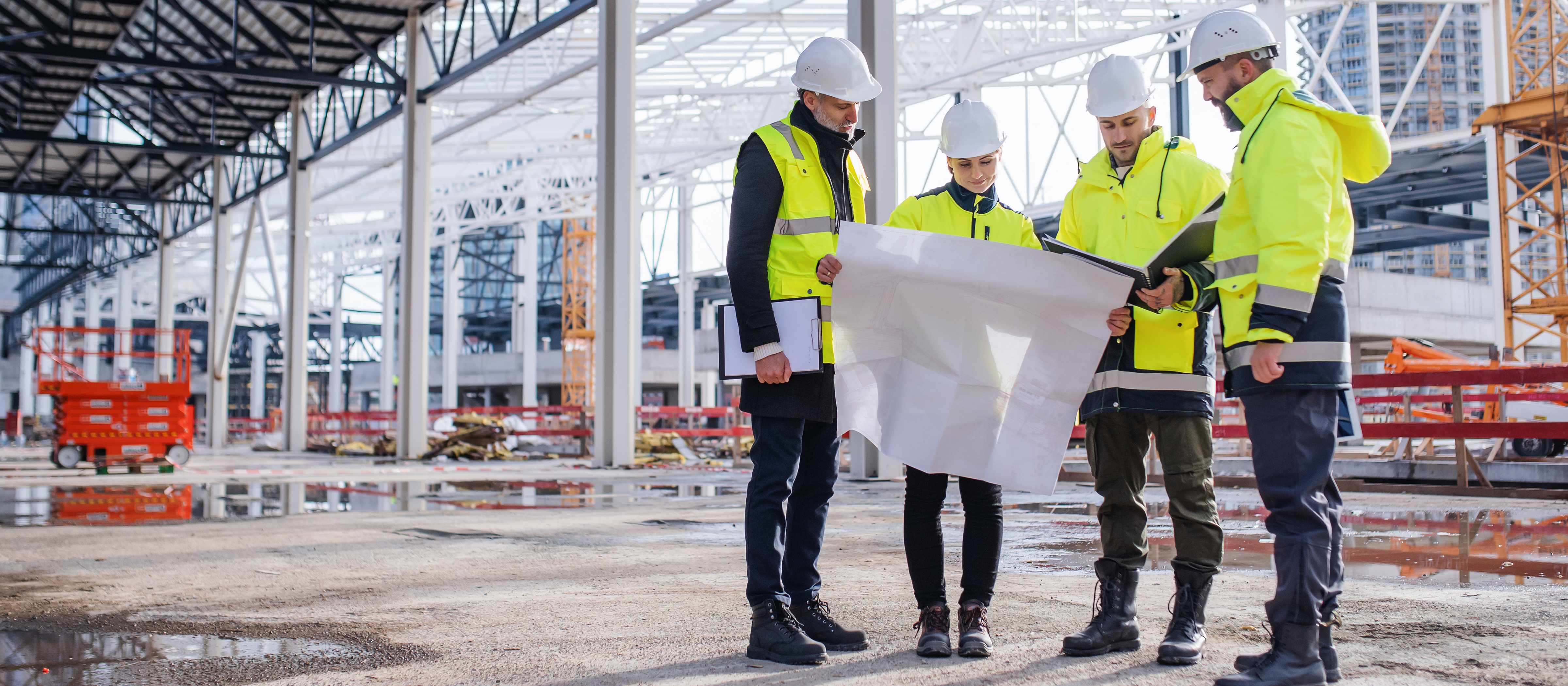 group of people wearing protective gear while looking at a paper in a constrution site 