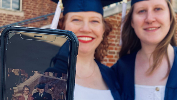 Two women in blue graduation caps and gowns with a cell phone showing an image.